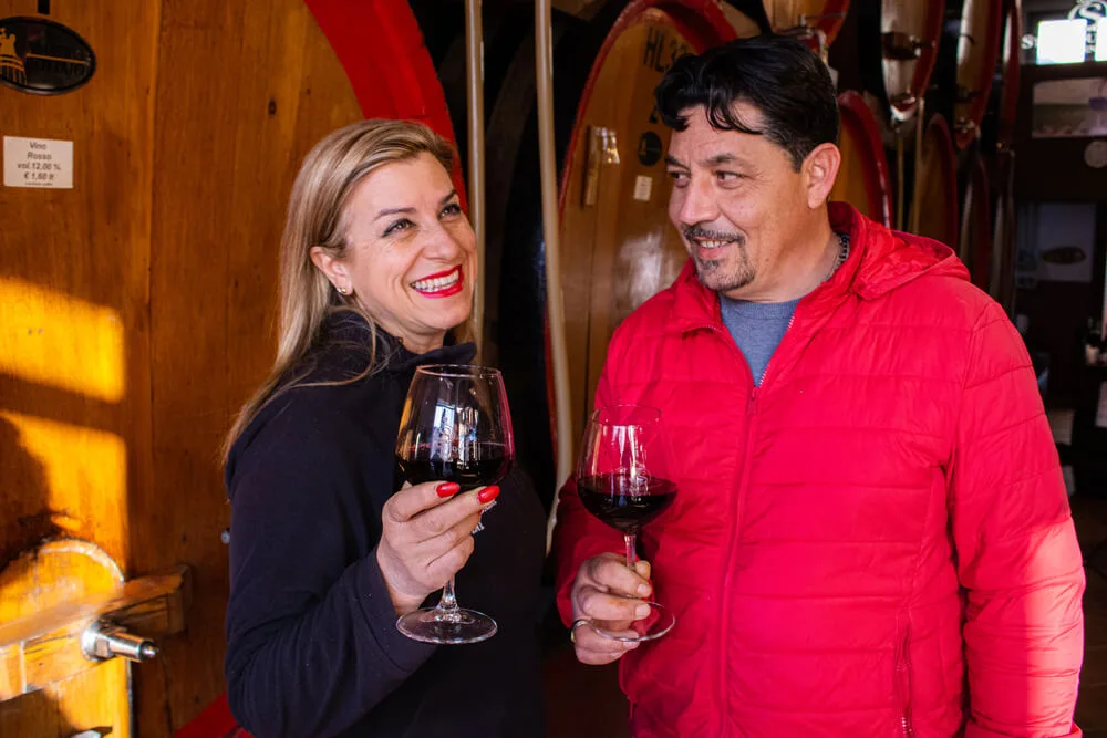 Coppia sorseggia vino rosso in cantina, tra botti di legno.